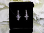 "J" hoop .25ct natural diamond earrings channel set in 10K white gold on a black pad with a white floral background.