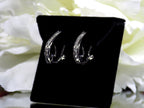 "J" hoop .25ct natural diamond earrings channel set in 10K white gold on a black pad with a white floral background. Side view.