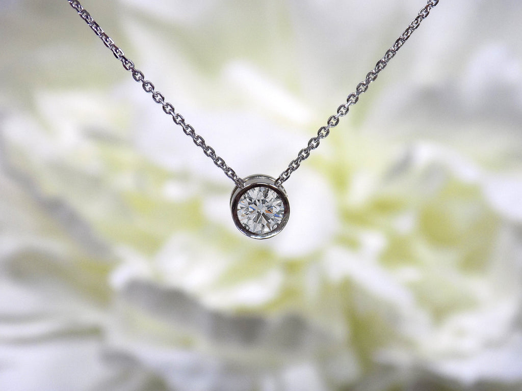 This is a bezel set slide .40ct natural diamond necklace in 14K white gold with a white floral background.
