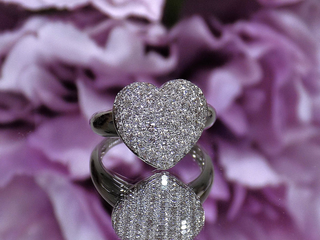 This is a 1.00ct heart shaped pave set natural diamond ring in 18K white gold on a mirrored surface with a purple floral background.
