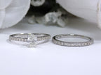 This shows both pieces of an oval shape diamond wedding set - the engagement ring laying beside its matching band with a white gold.