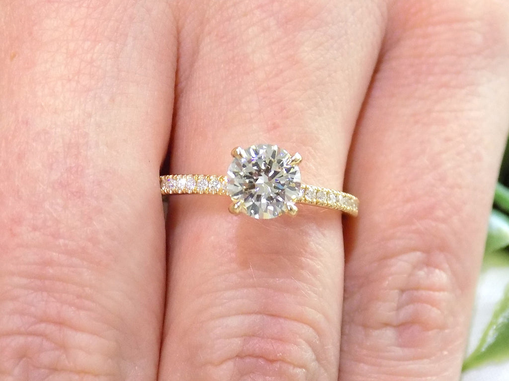 This is a women's natural round brilliant diamond ring with a 1.02ct center and .23ct in accents diamonds set in yellow gold shown on a woman's finger.