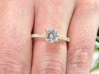 This is a women's natural round brilliant diamond ring with a 1.02ct center and .23ct in accents diamonds set in yellow gold shown on a woman's finger.