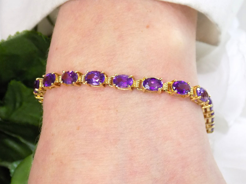 This is a women's straight line oval shape 10ct total weight natural amethyst bracelet in 14K yellow gold on a women's wrist.