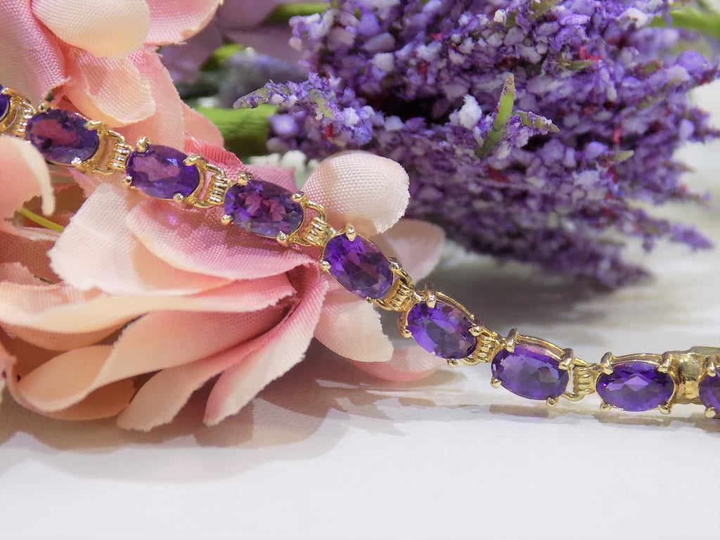 This is a women's straight line oval shape 10ct total weight natural amethyst bracelet in 14K yellow gold with a floral background.