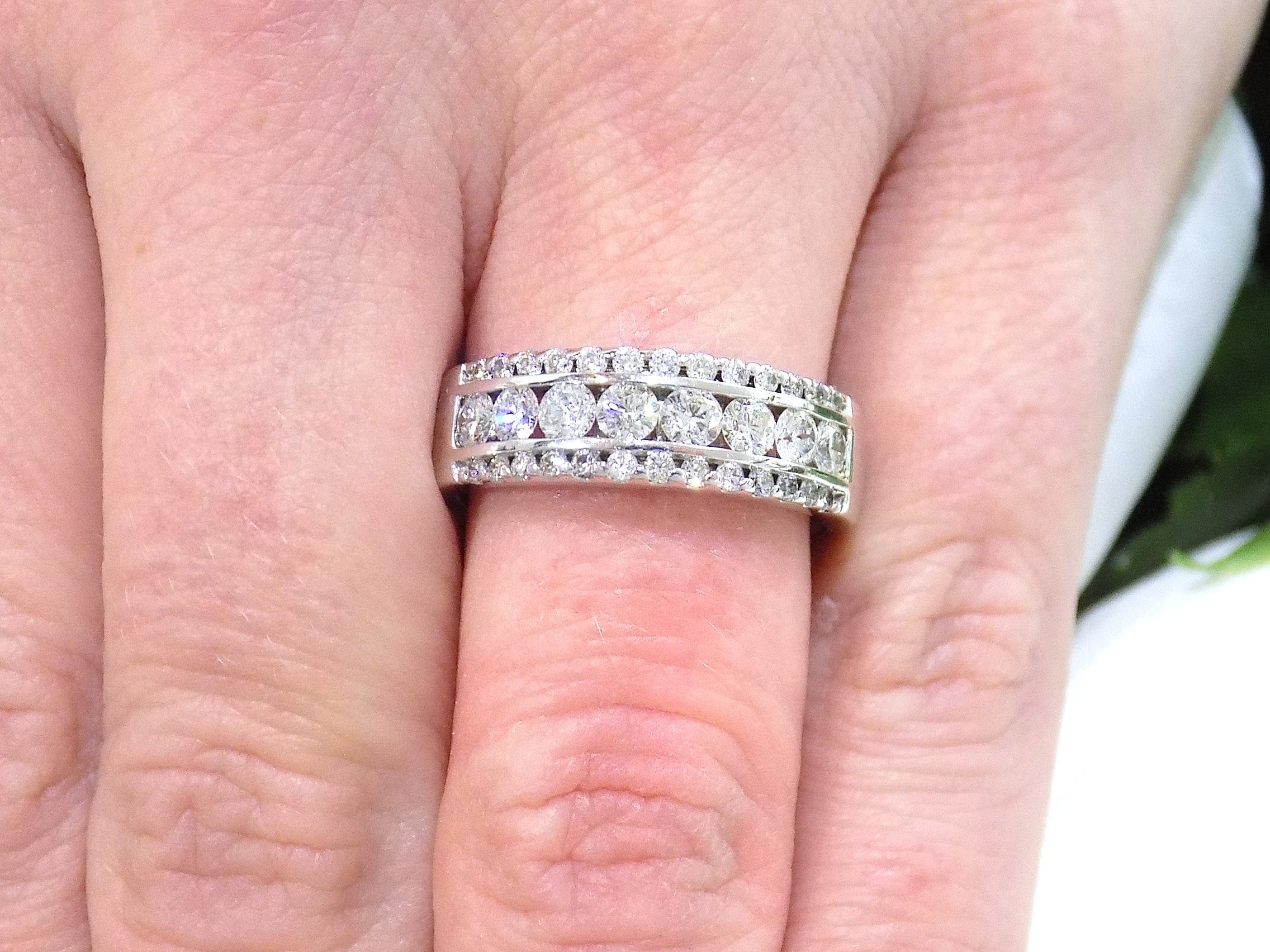 This is 3-row channel & prong set 1.00ct total weight natural wide diamond band in white gold shown on a woman's finger.