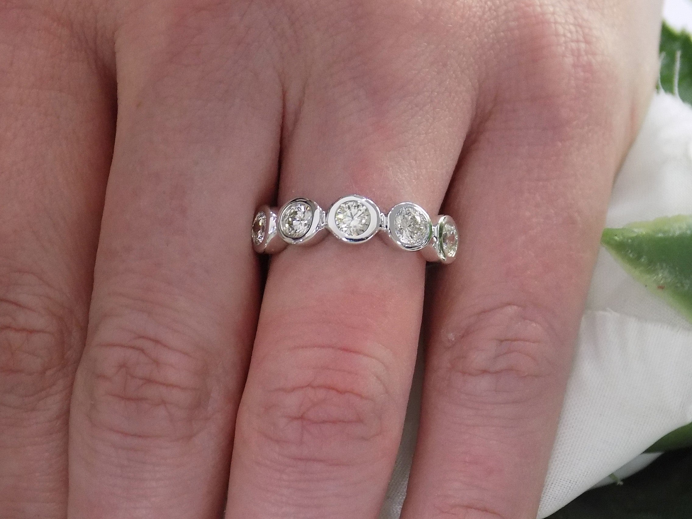 This is a 5 stone bezel set natural round diamond band in 14K white gold on a woman's finger.