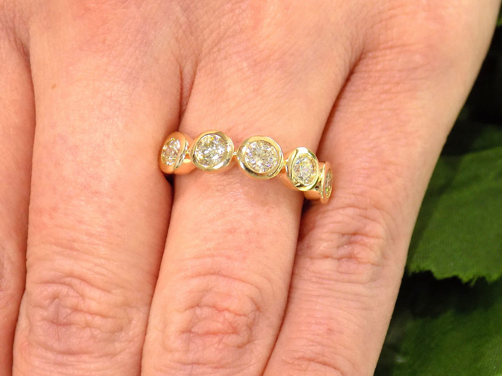 This is a bezel set 5-stone natural 1ct total weight diamond band in yellow gold shown on a woman's finger.