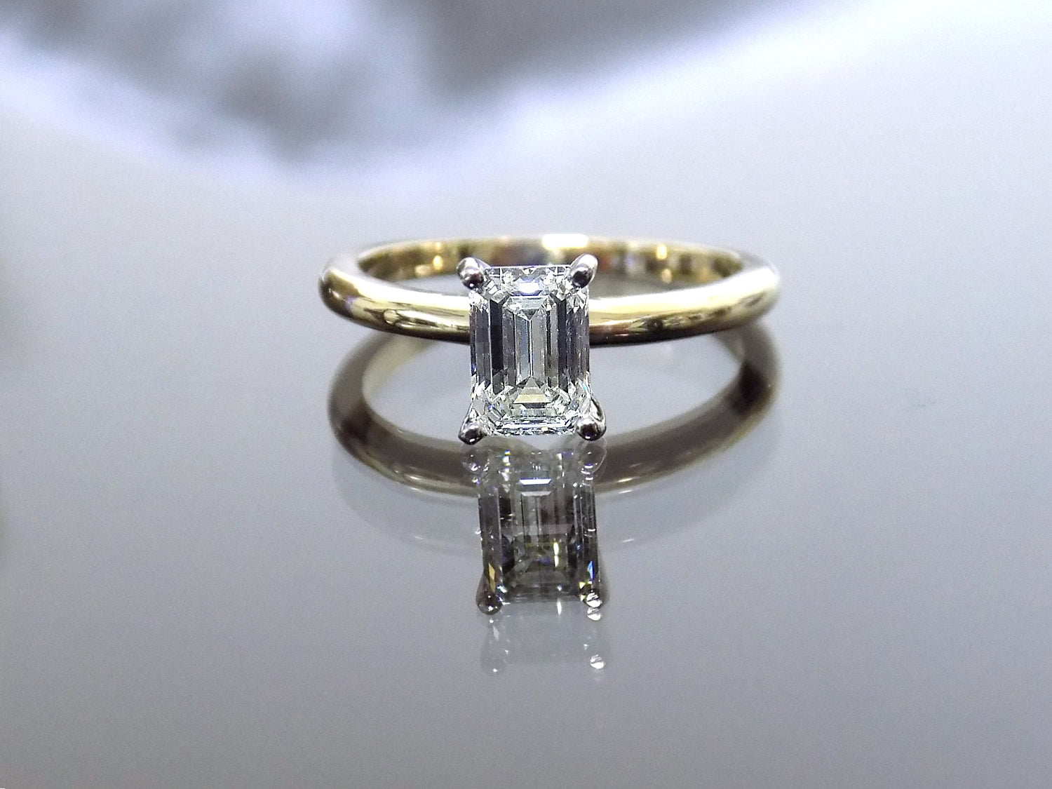 This is a ladies' 1.11ct emerald cut natural diamond solitaire ring in yellow gold with mirrored background.