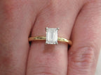 This is a ladies' 1.11ct emerald cut natural diamond solitaire ring in yellow gold shown on a woman's finger.