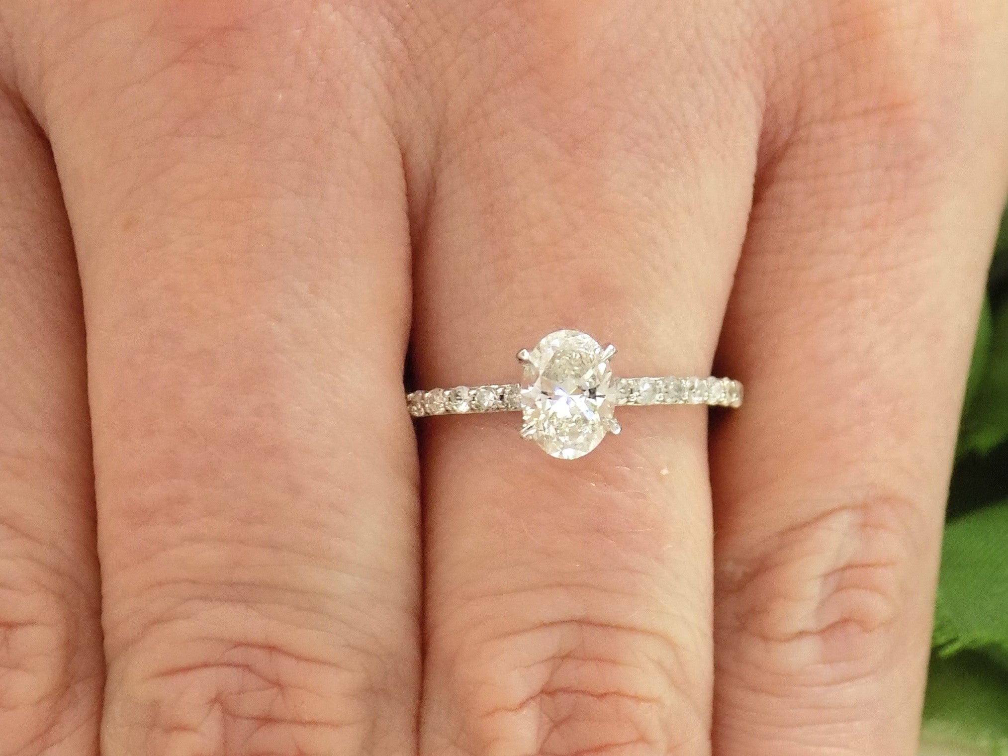 This a 1ct total weight natural oval shape diamond set on a straight line diamond band in white gold shown on a woman's finger.