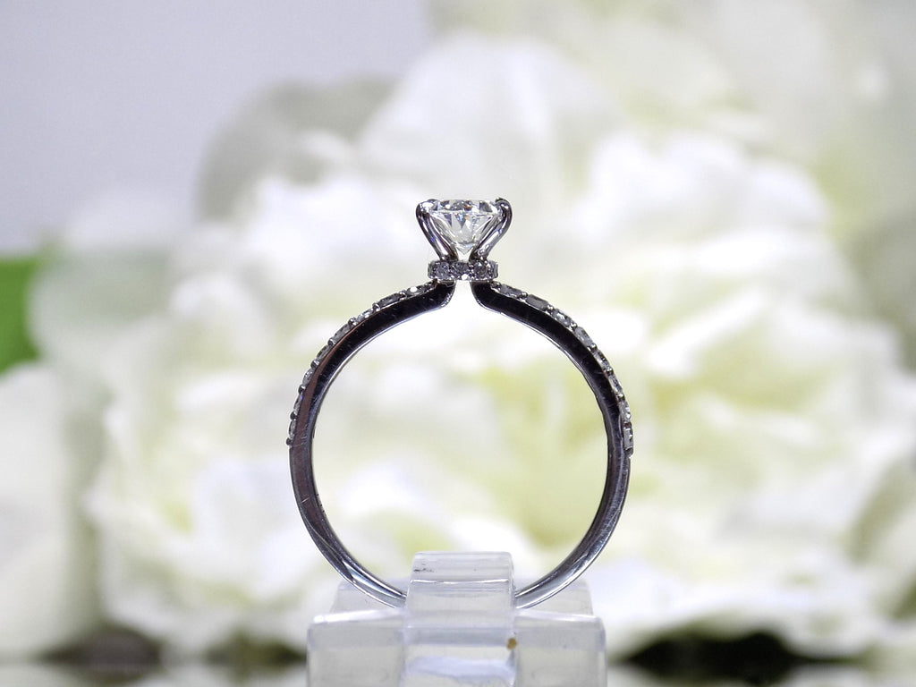 This a side view of a 1ct total weight natural oval shape diamond set on a straight line diamond band in white gold with a white flowery backgound.