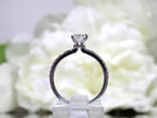 This a side view of a 1ct total weight natural oval shape diamond set on a straight line diamond band in white gold with a white flowery backgound.