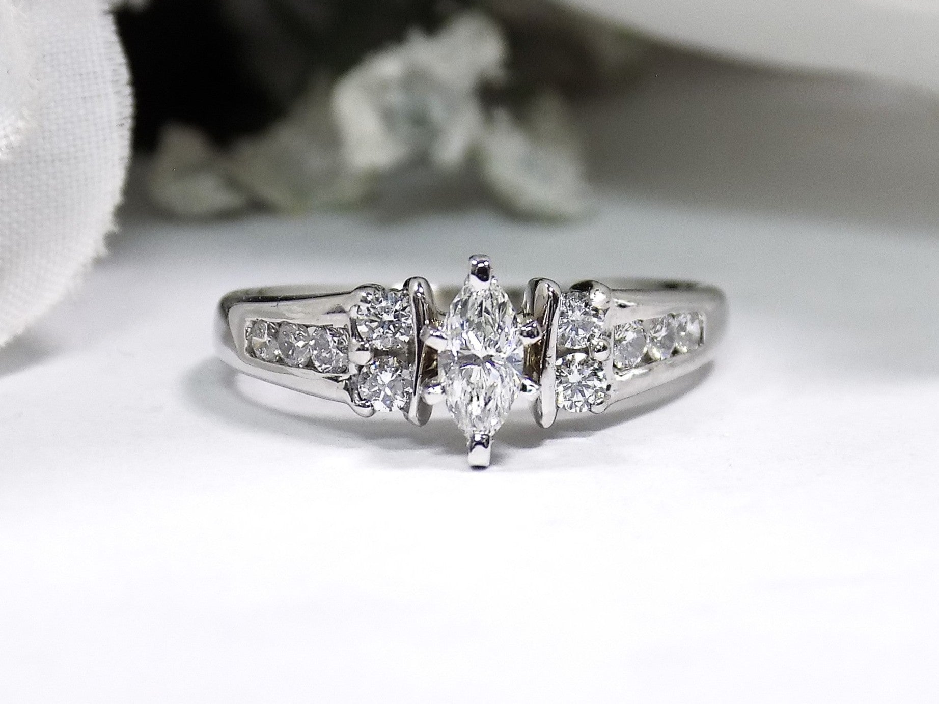 This is a marquise shape diamond ring with round diamond accents in white gold with a white background.