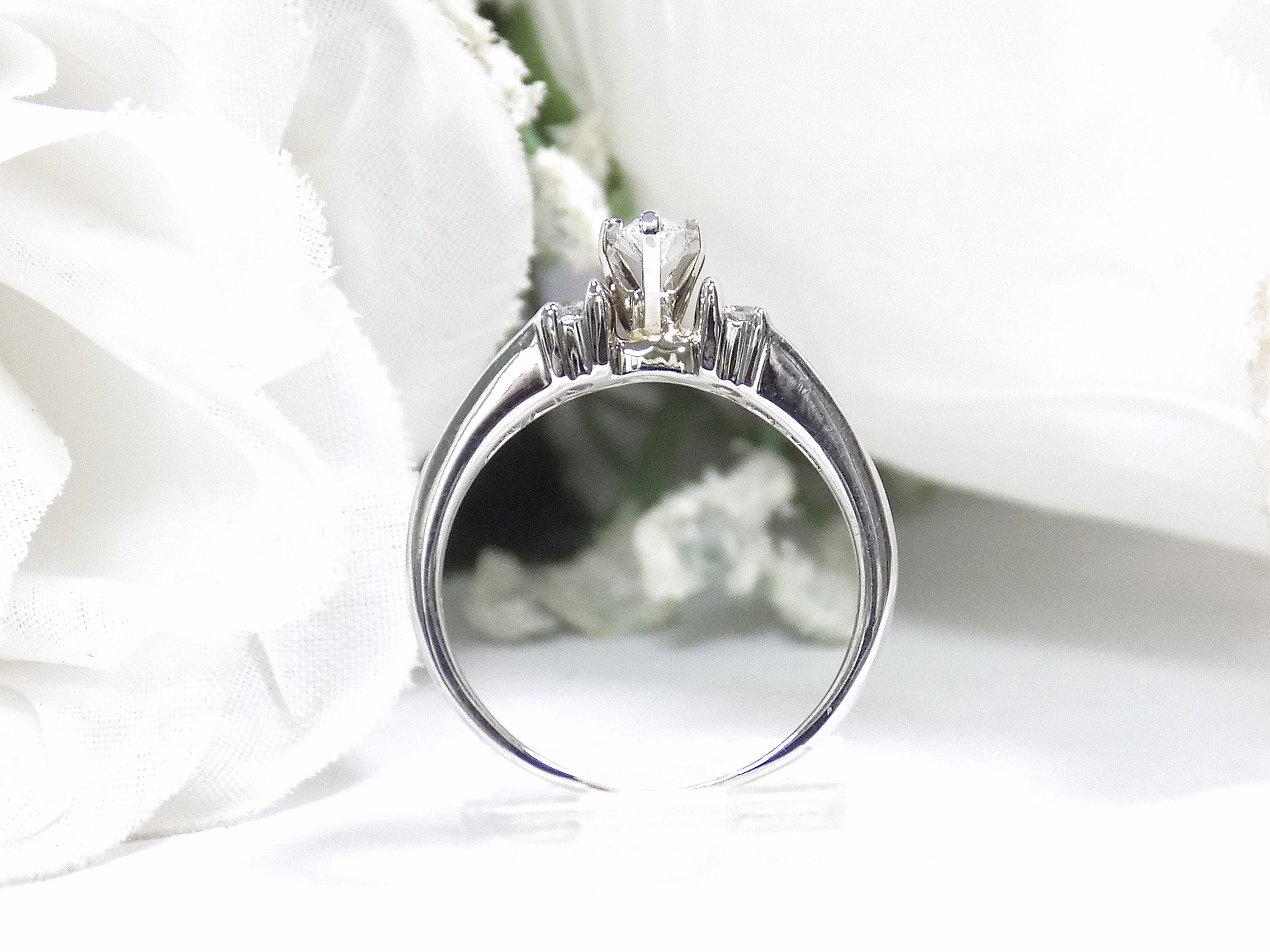 This is a marquise shape diamond ring with round diamond accents in white gold shown from the side with white background.