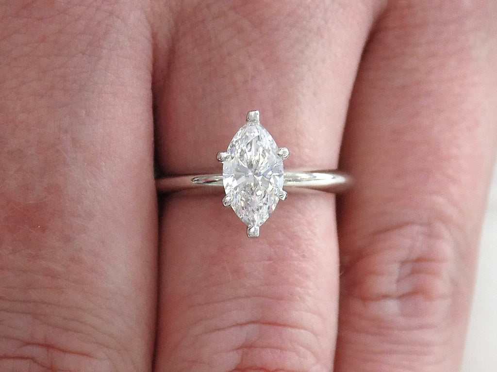 This is a 1ct marquise shape diamond solitaire ring in white gold shown on a woman's finger.