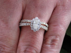 This is 2-piece natural oval shape diamond wedding set weighing 1ct total with both the engagement ring and matching band in yellow gold with white gold prongs and shown on a woman's finger.