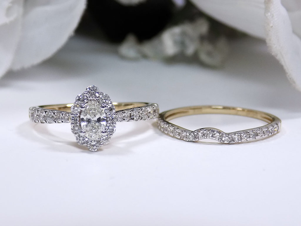 This is 2-piece natural oval shape diamond wedding set weighing 1ct total with both the engagement ring and matching band in yellow gold with white gold prongs laying side by side and a white background.