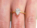 This is high quality 1.00ct natural pear shape diamond solitaire ring in yellow gold shown on a woman's finger.