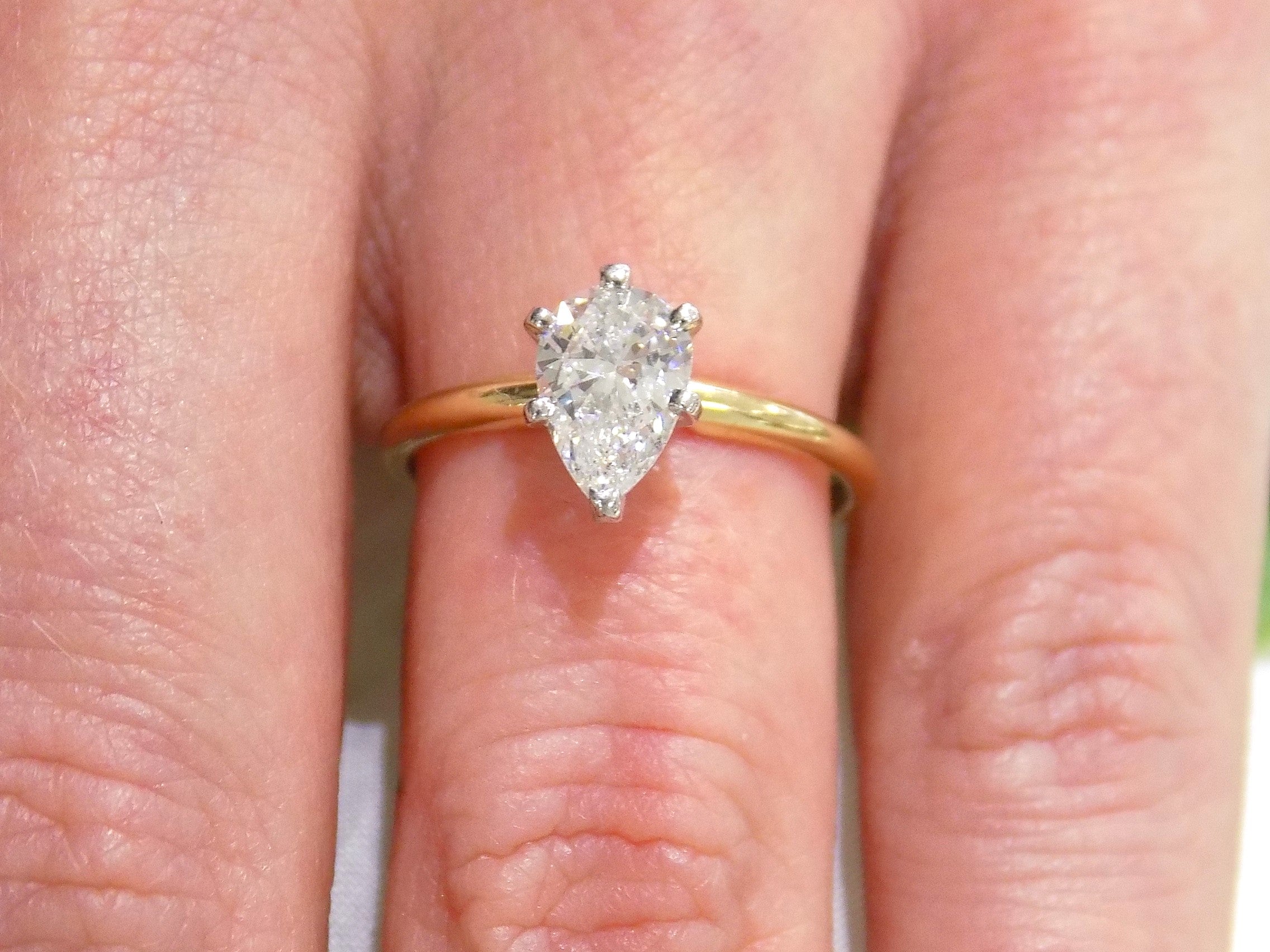 This is high quality 1.00ct natural pear shape diamond solitaire ring in yellow gold shown on a woman's finger.