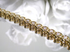 This is a 2.00ct total weight diamond bracelet in 14K yellow gold on a mirror with a white floral background.