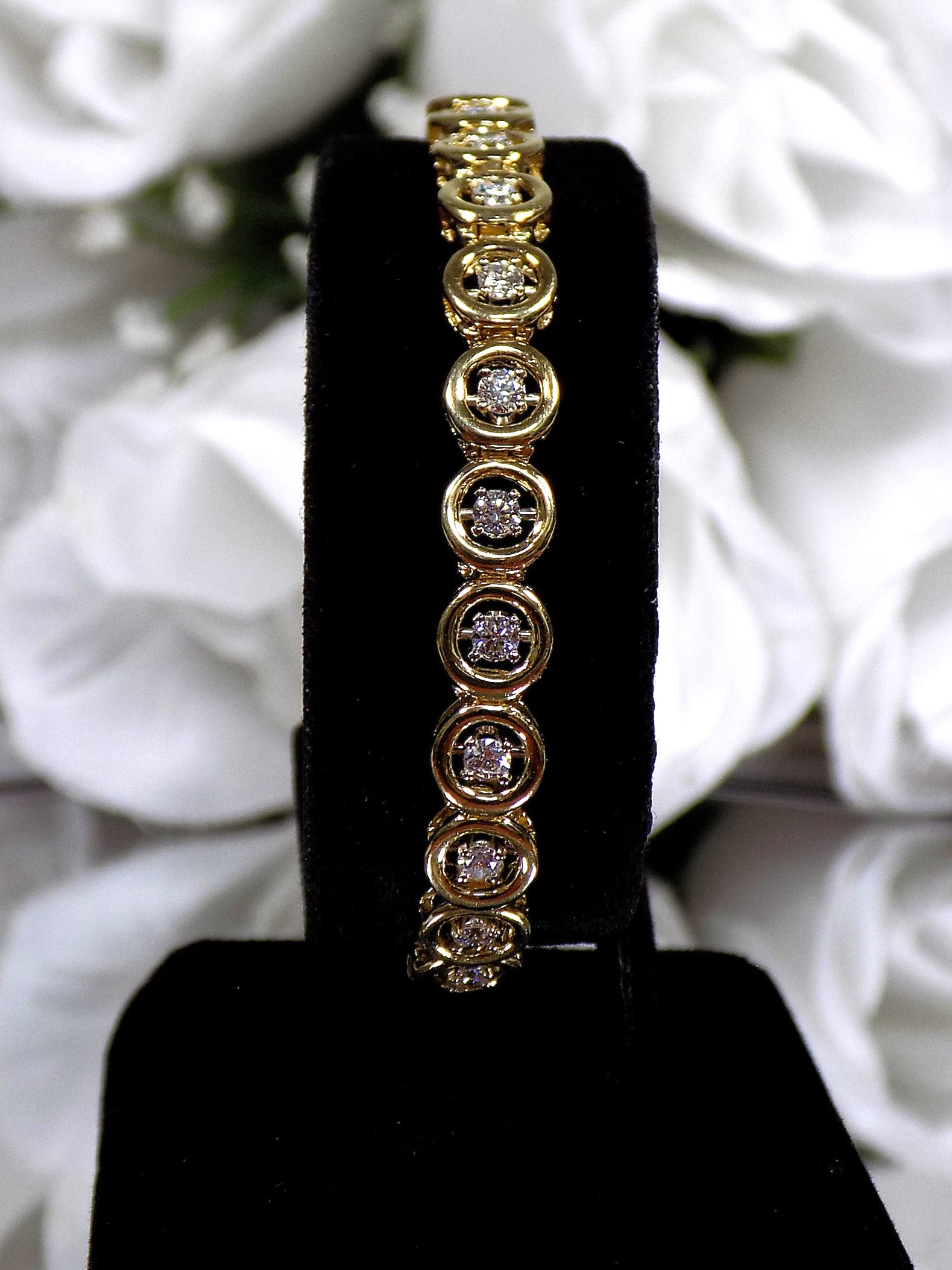 This is a 2.00ct total weight diamond bracelet in 14K yellow gold on a black stand with a white floral background.