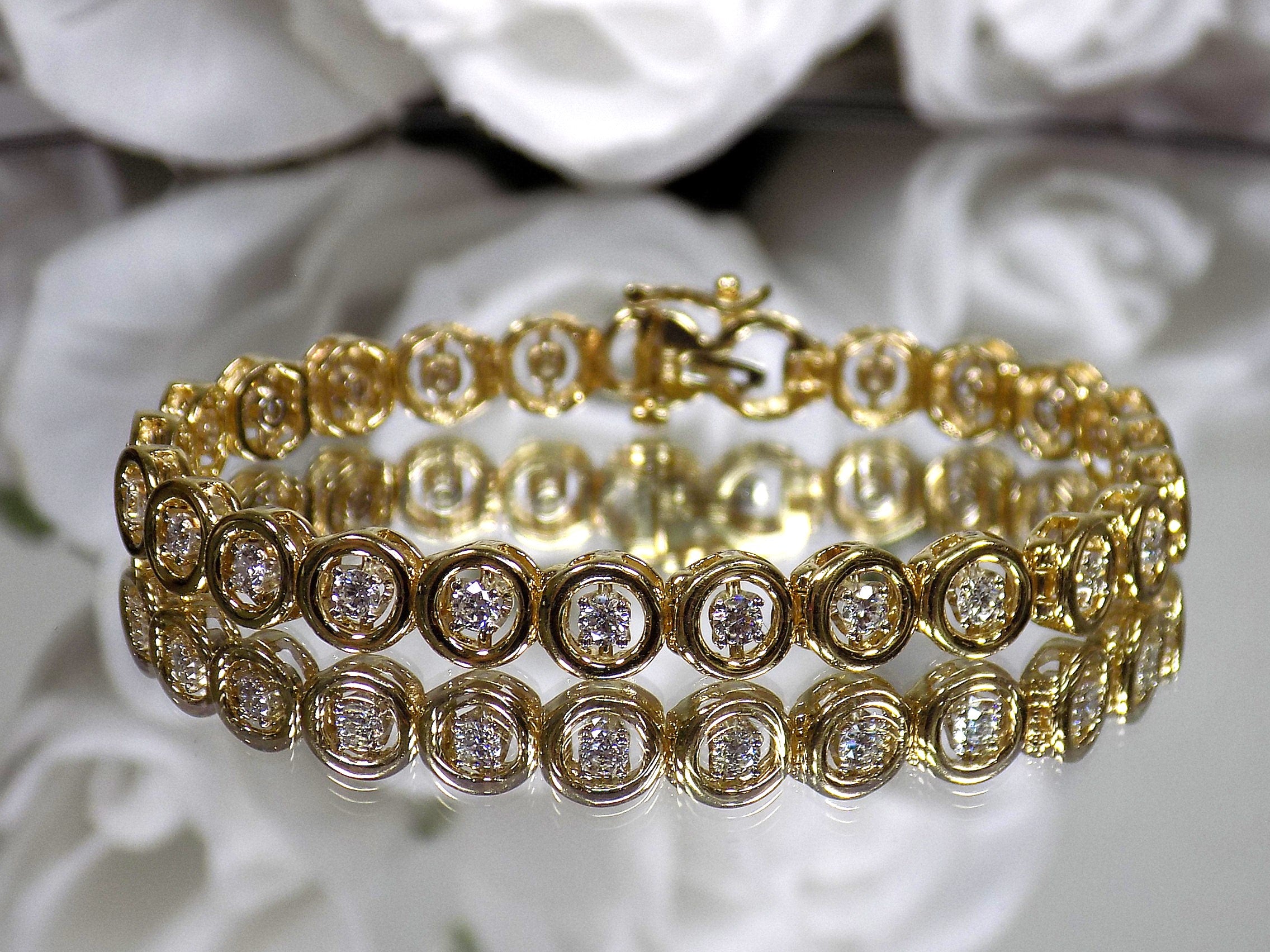 This is a 2.00ct total weight diamond bracelet in 14K yellow gold on a mirror with a white floral background.