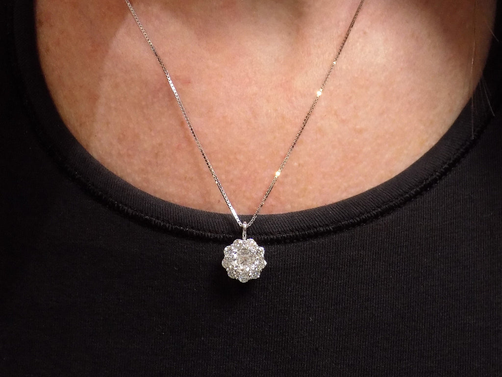 This is a 2.00ct natural round halo style diamond necklace with a 1.00ct center round brilliant diamond and 1.00ct round brilliant diamonds in the halo in 14K white gold on a ladies neck with a black top.