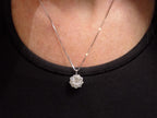 This is a 2.00ct natural round halo style diamond necklace with a 1.00ct center round brilliant diamond and 1.00ct round brilliant diamonds in the halo in 14K white gold on a ladies neck with a black top.