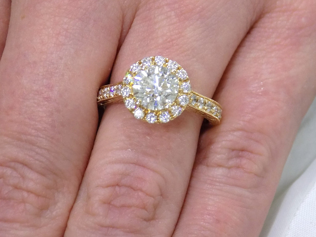 This is halo style 2.17ct total weight natural round diamond ring with a 1.52ct center diamond in yellow gold shown on a ladies' finger.