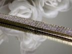 This is a 22.00ct natural princess cut diamond bracelet with 76.4 grams of 18K yellow gold on a mirrored surface with a white floral background.