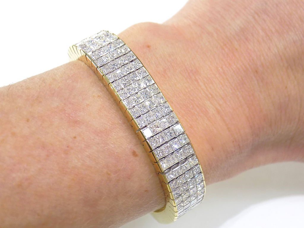 This is a 22.00ct natural princess cut diamond bracelet with 76.4 grams of 18K yellow gold on a ladies wrist with a white background.