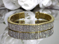 This is a 22.00ct natural princess cut diamond bracelet with 76.4 grams of 18K yellow gold on a mirrored surface with a white floral background.
