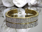 This is a 22.00ct natural princess cut diamond bracelet with 76.4 grams of 18K yellow gold on a mirrored surface with a white floral background.