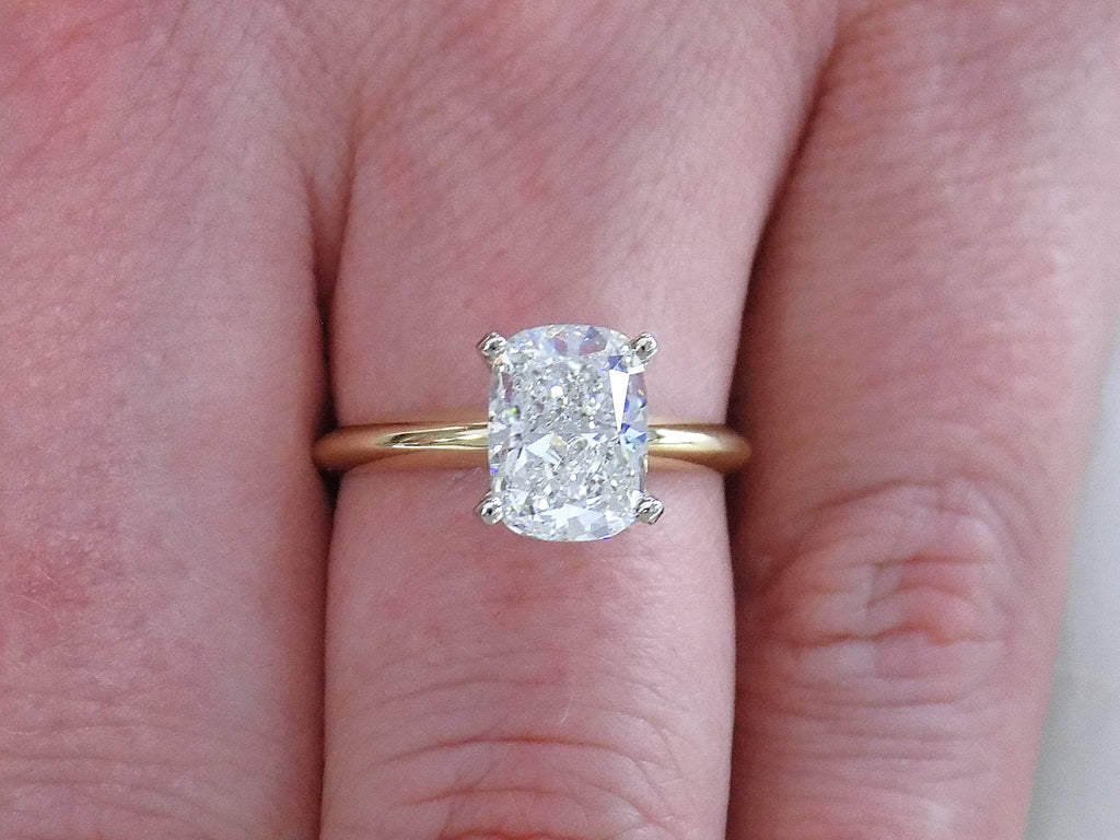 This is a 2.01ct natural elongated cushion cut diamond solitaire in yellow gold shown on a woman's finger.