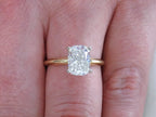 This is a 2.01ct natural elongated cushion cut diamond solitaire in yellow gold shown on a woman's finger.