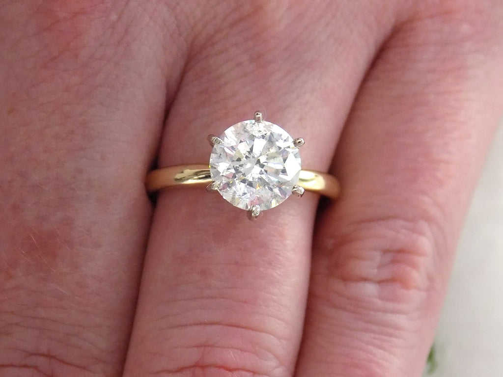 This is a 2.20ct natural round brilliant diamond solitaire in yellow gold shown on a woman's finger.