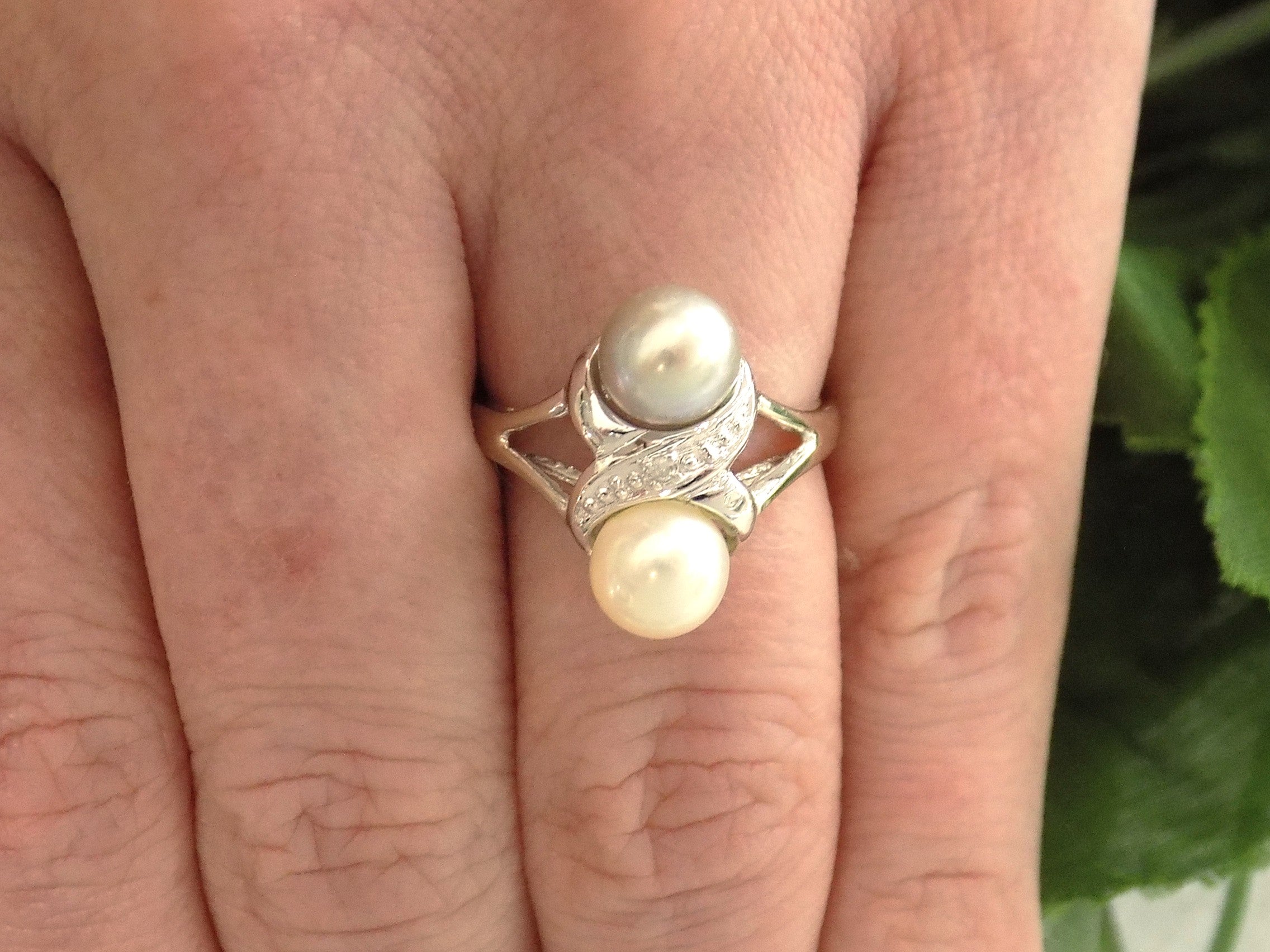 This is fully restored like new 2-pearl ring one gray and one white pearl with diamond accents shown on a woman's finger.