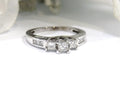 This is a 1.00ct total weight 3-stone princess cut diamond ring with channel set princess cut diamonds down the side in 14K white gold on a white background.