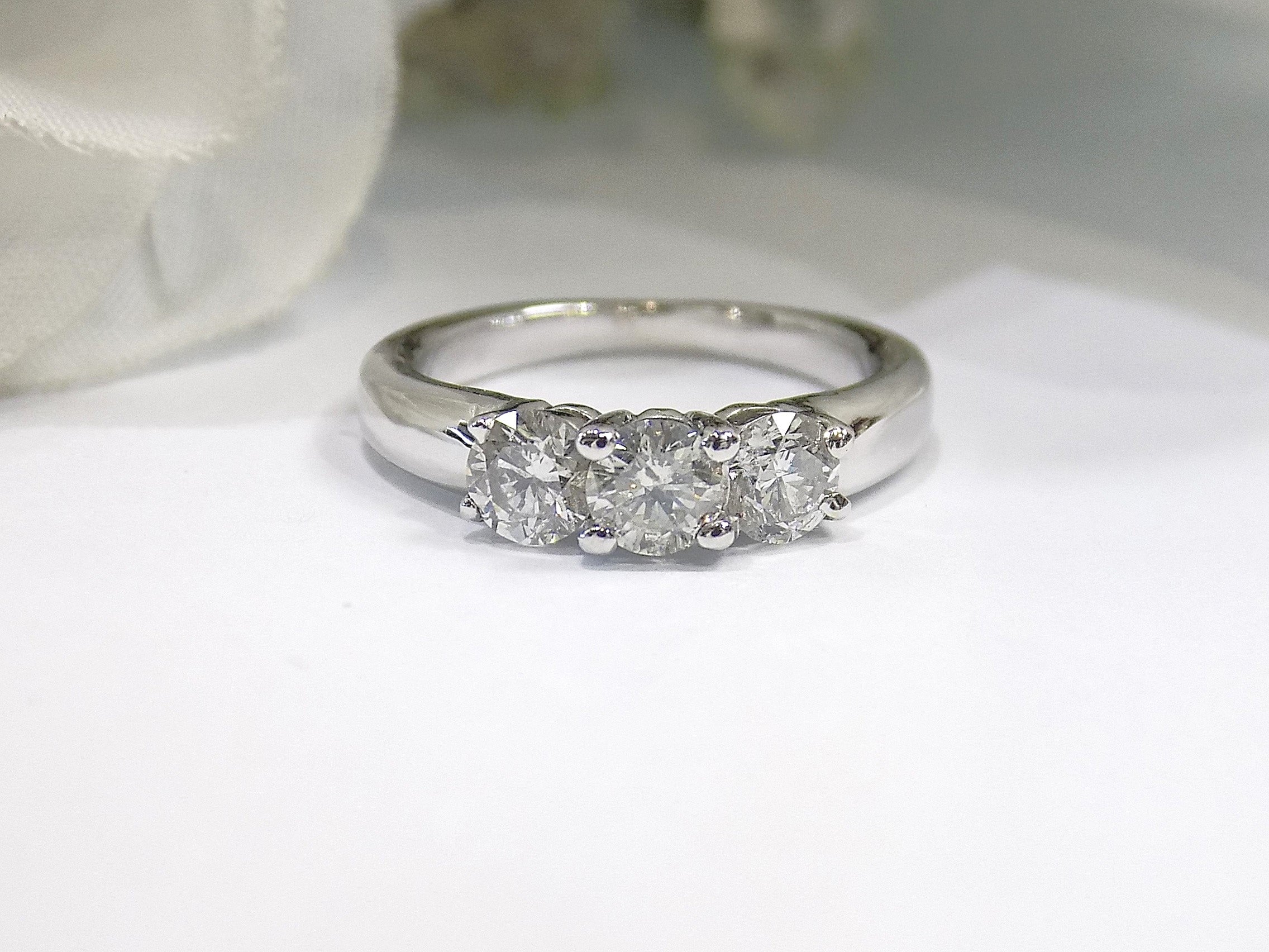 This is a 3-stone style natural .90ct total weight round diamond ring in white gold with a white background.