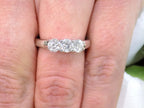 This is a 3-stone style natural .90ct total weight round diamond ring in white gold shown on a woman's finger.