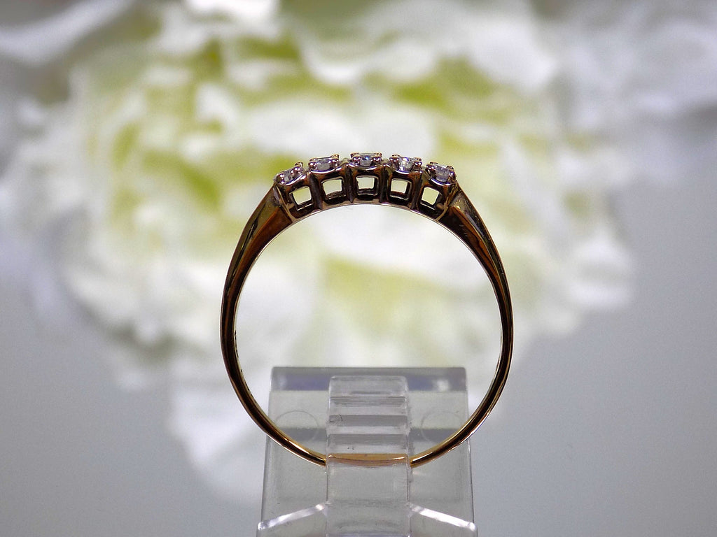 This is a side view of a preowned or estate small 5-stone natural diamond band in yellow gold with a flowery background.
