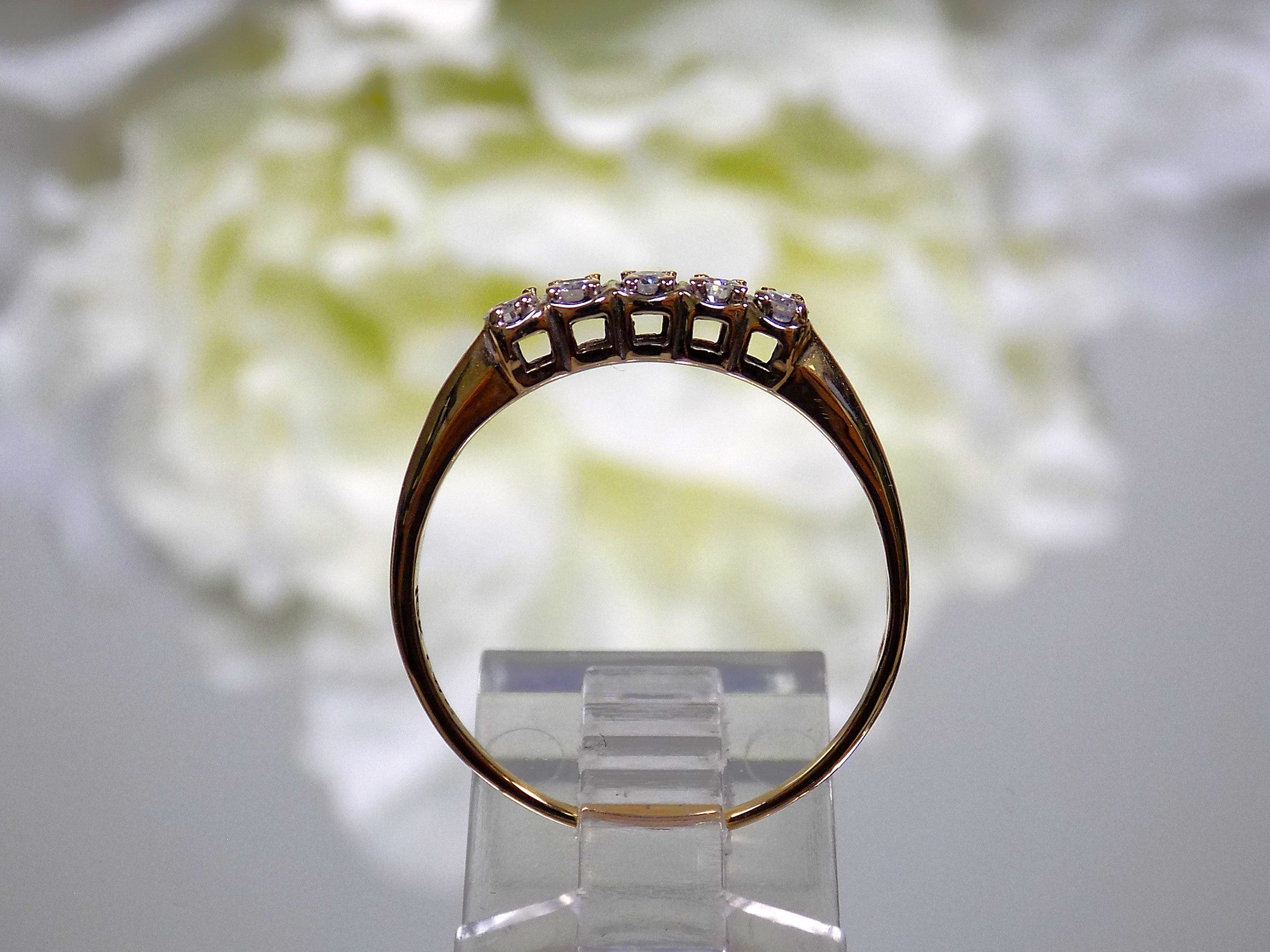 This is a side view of a preowned or estate small 5-stone natural diamond band in yellow gold with a flowery background.