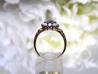 This a side view of a ring with an oval blue topaz in the center and surrounded by natural opals in yellow gold from our estate collection with a flowery background.