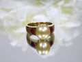 This is a women's vintage ring with center 9mm golden akoya cultured pearl and 2 .25ct bezel set natural rubies in 18K yellow gold on a mirrored surface with and white floral background.