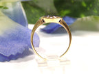 This is a vintage oval bezel set black onyx ring in 10K yellow gold.  It is 21mm long and 18mm wide side view on a white surface with a blue floral background.