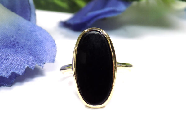 This is a vintage oval bezel set black onyx ring in 10K yellow gold.  It is 21mm long and 18mm wide on a white surface with a blue floral background.