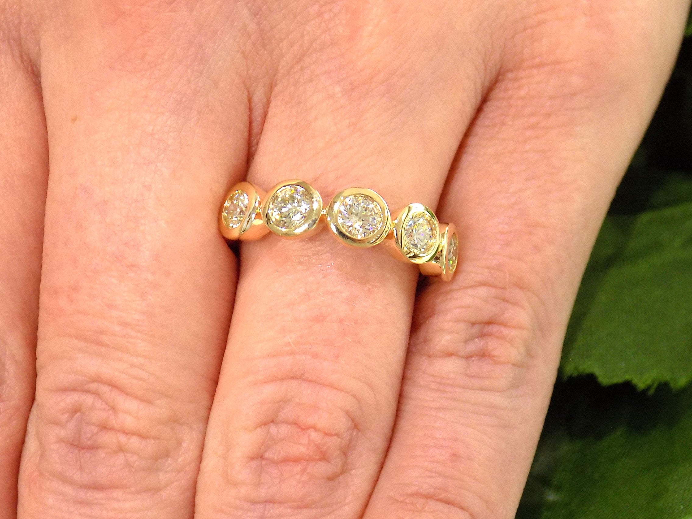 This is a 5 stone bezel set natural round diamond band in 14K yellow gold on a ladies finger.