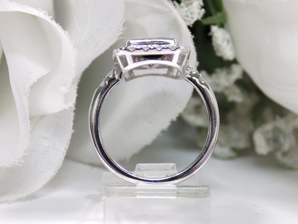This is a women's ring with a natural 2.66ct bi-color tourmaline.  It's colors are a deep rich blueish green on one end that turns to a vivid pink on the other side.  The tourmaline is surrounded by .66ct in natural round accent diamonds in 14K white gold on a white surface with a white floral background from a side view.
