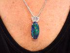 This is a women's 7.48ct total weight natural black opal and baguette diamond pendant or necklace in white gold shown on a women's neck.